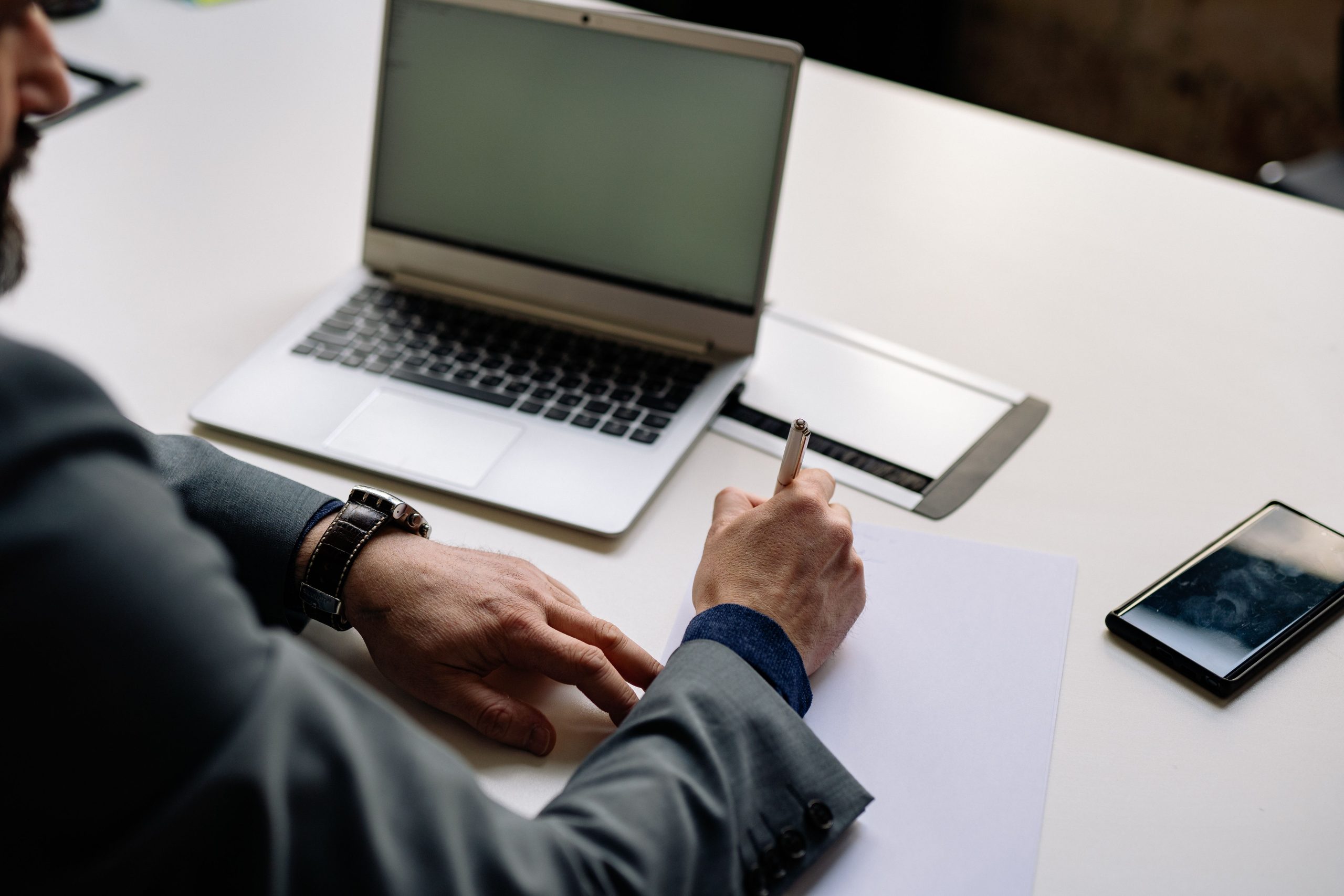 Professionnel écrivant notes avec laptop et téléphone